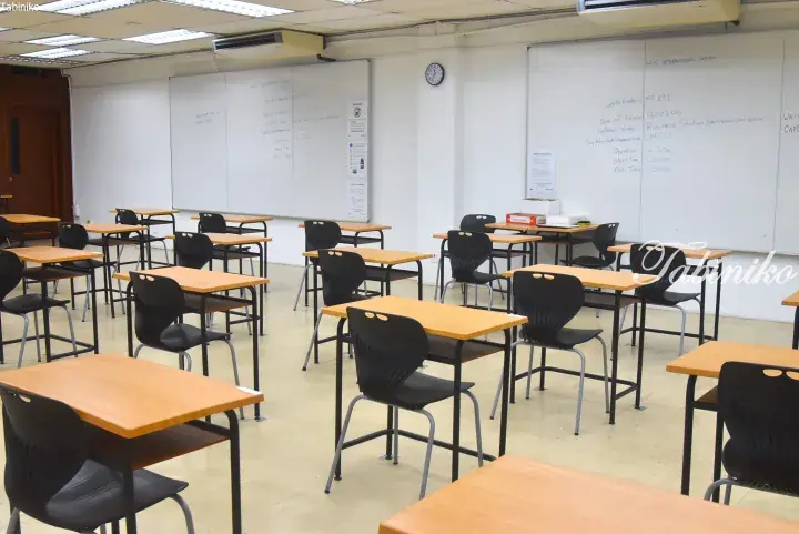 Empty exam hall at HIS International School with desks and whiteboards showing Business Studies exam details.