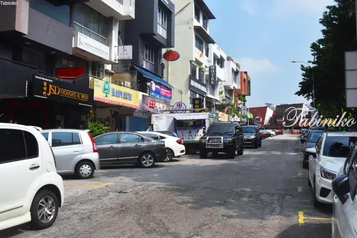 Street view of shops and parked cars in Malaysia, featuring a liquor store and copy center.