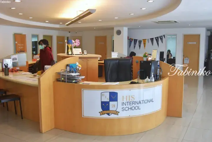 Reception desk of HIS International School featuring a wooden counter, school crest, and office staff.