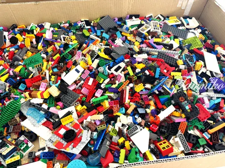A cardboard box filled with a colorful assortment of loose LEGO bricks and building pieces.