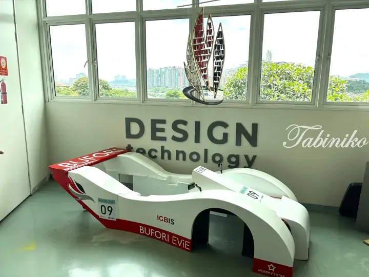 White and red Bufori EViE electric vehicle displayed in a Design Technology room with city view.