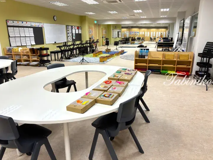 Spacious music classroom with white table displaying colorful bead crafts, keyboards, xylophones, and musical instruments.