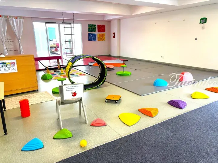 Colorful sensory play area with balance equipment, mats, and a tunnel in a bright indoor space.