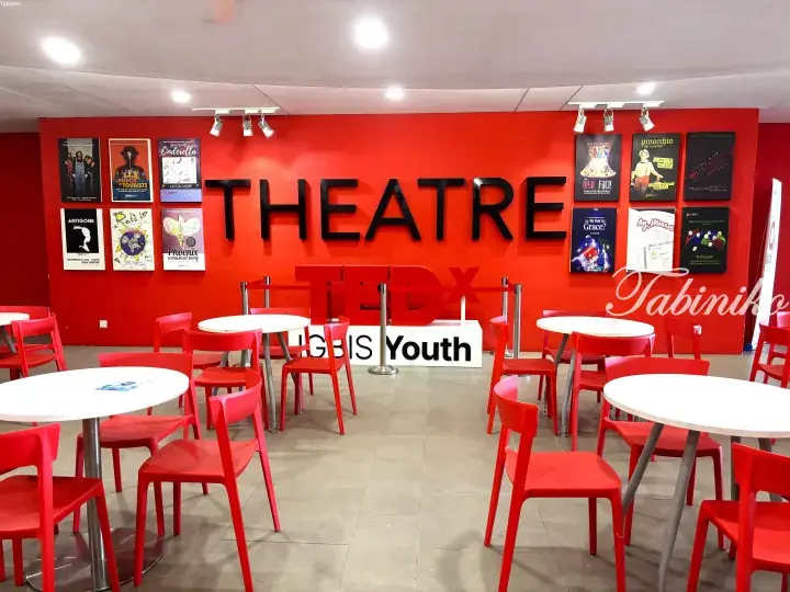 Red and white seating area with TEDx IGBIS Youth sign and theatre posters on a bright orange wall.