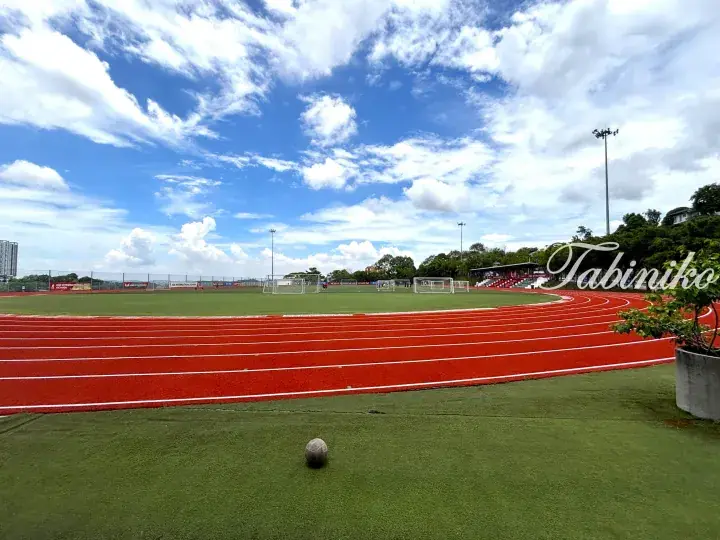 Red running track surrounding green football field at IGB International School under blue sky
