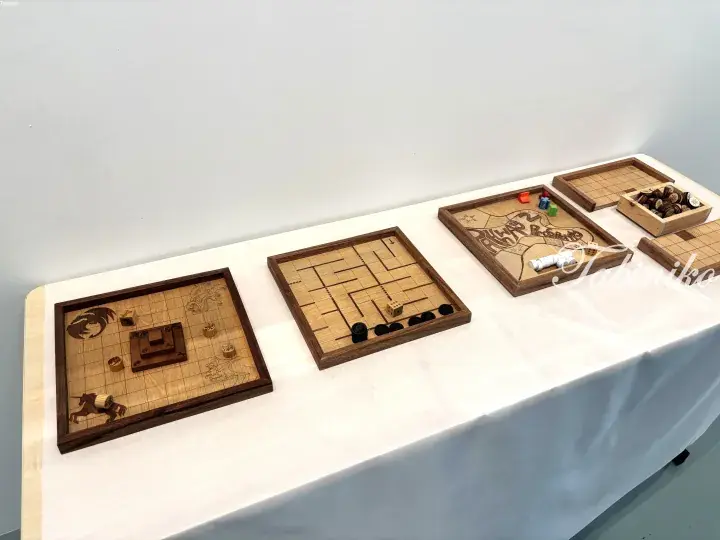 Handcrafted wooden board games displayed on a white table, featuring intricate designs and game pieces.