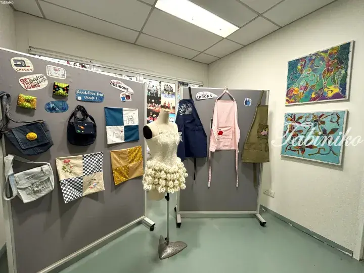 Display of student sewing projects including bags, aprons, and a dress on mannequin at a school exhibition.