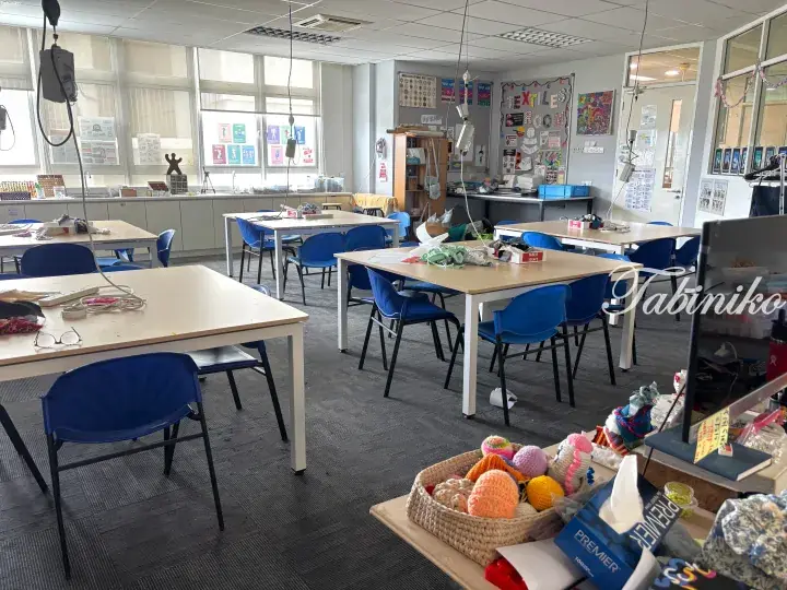 Bright textile classroom with blue chairs, tables, and colorful yarn crafts.