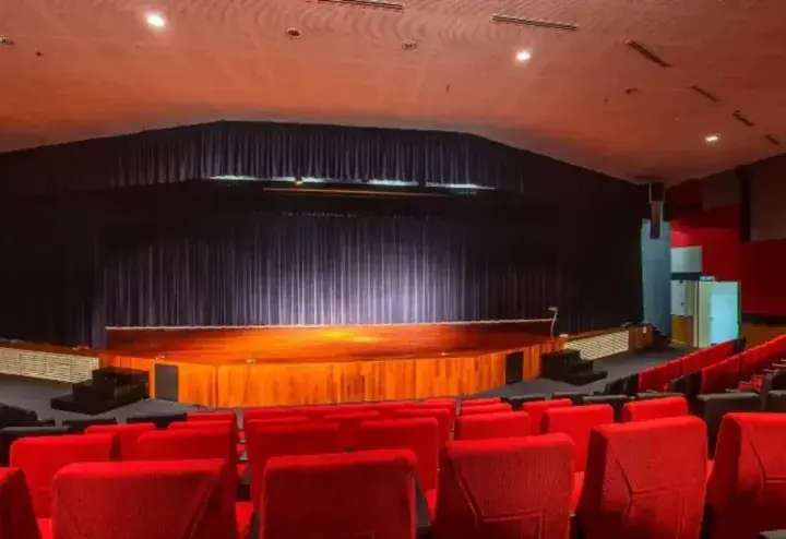 Interior view of a modern auditorium with red seats and a wooden stage under a curved ceiling.