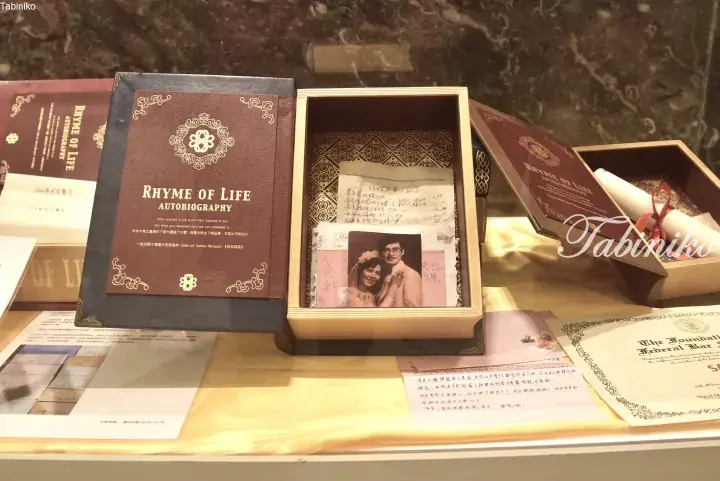 A display case featuring a “Rhyme of Life” autobiography book and a wooden box containing a vintage wedding photo and handwritten notes.