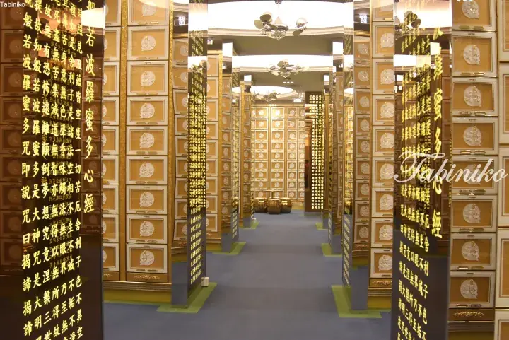 Interior of a modern columbarium with golden niches and black pillars inscribed with the Heart Sutra.