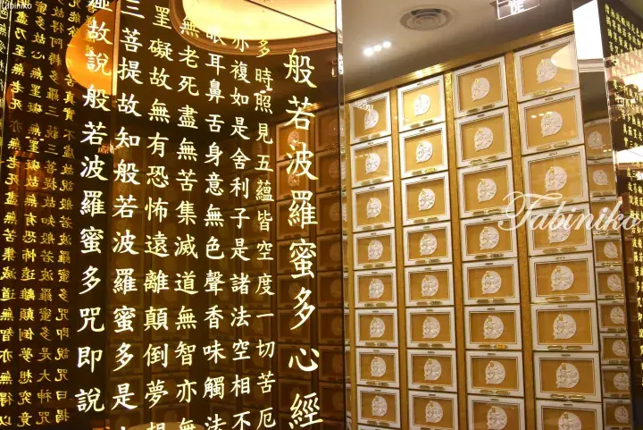 Interior of a Buddhist temple featuring a golden wall with the Heart Sutra text and rows of memorial niches.