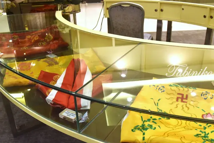 Traditional Chinese ceremonial textiles with gold thread crane blankets displayed in a glass showcase.