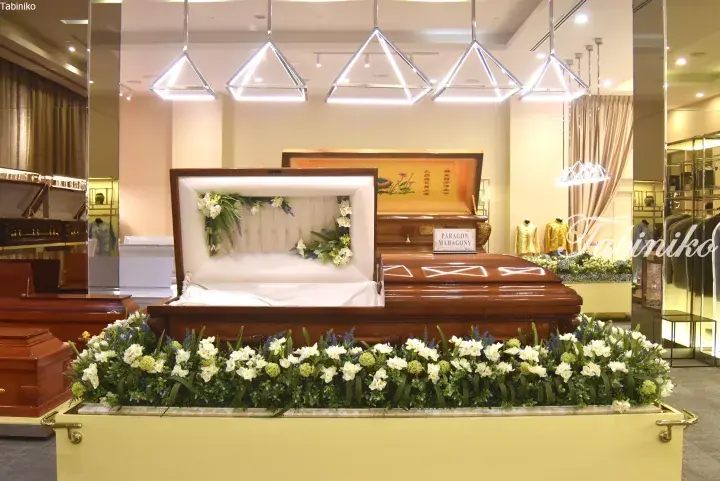 Elegant mahogany coffin with white interior and floral arrangement displayed in a modern funeral home showroom.