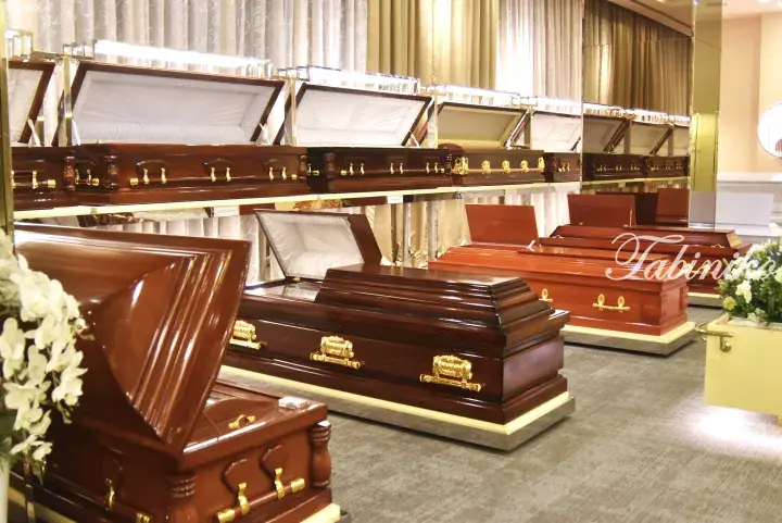 Rows of polished wooden coffins with gold handles displayed in a funeral home showroom.