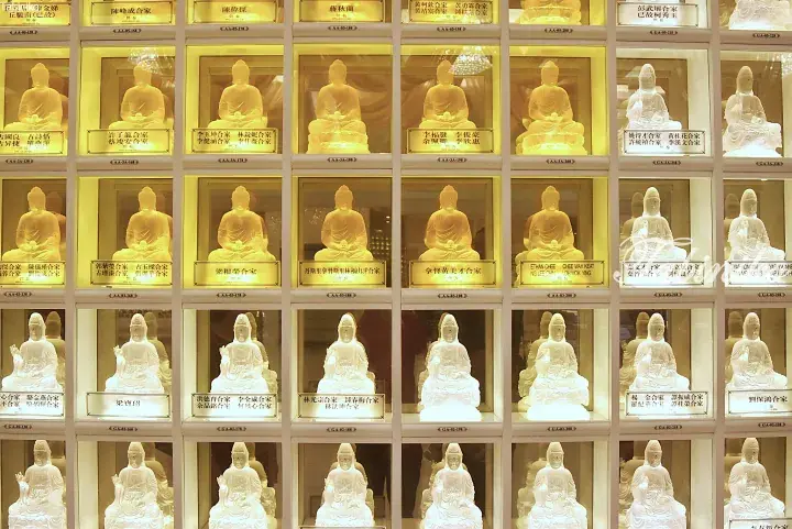 Rows of illuminated niches in a Malaysian columbarium, each housing a Buddha or Guanyin statue with donor nameplates.