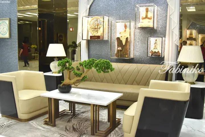 Elegant hotel lobby with cream leather sofas, a bonsai tree, and framed Buddha statues displayed on a sparkling blue wall.
