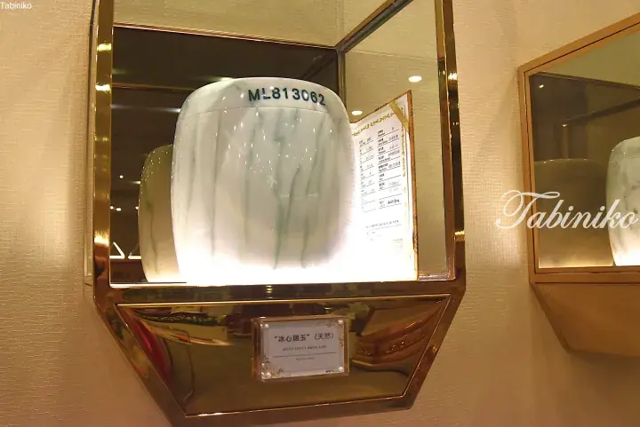 A white jade urn labeled ML813062 displayed in a glass case with a certificate and a plaque reading “Ice Heart Auspicious Jade”.