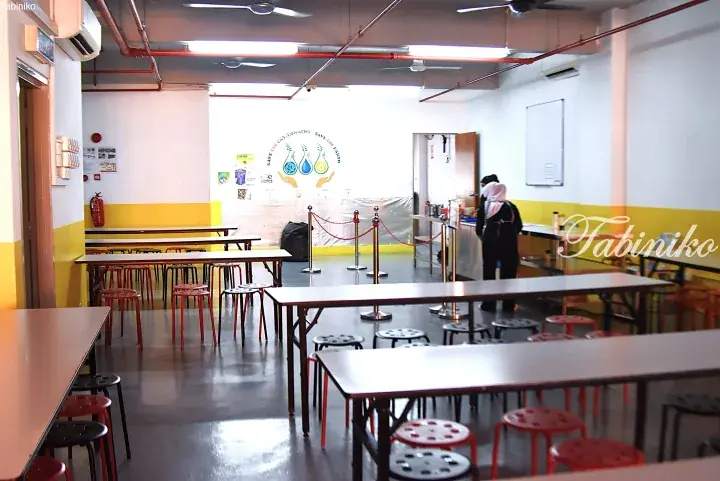 Bright cafeteria with long tables, red stools, and a &ldquo;Save the Earth&rdquo; wall mural in a Malaysian property.