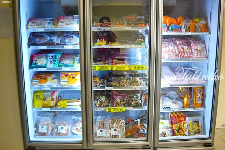 Glass-door freezers stocked with frozen dumplings, sausages, and meat at a Malaysian supermarket.