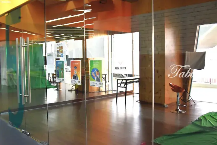 Glass entrance to Edu Talent with safety posters and green screen setup inside.