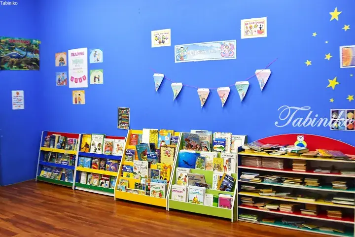 Colorful children&rsquo;s bookshelves and reading corner with motivational posters on a blue wall.