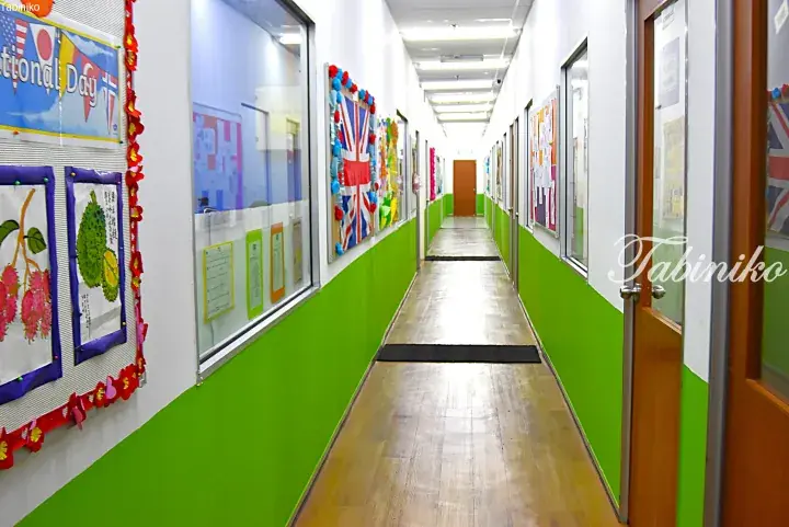 Bright school hallway with green walls, wooden floors, and student artwork displayed on notice boards.