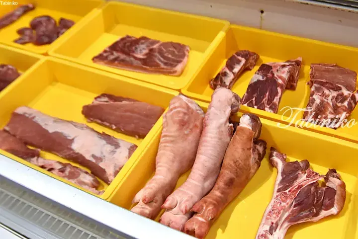 Various cuts of raw pork, including trotters and ribs, displayed in yellow trays at a market.