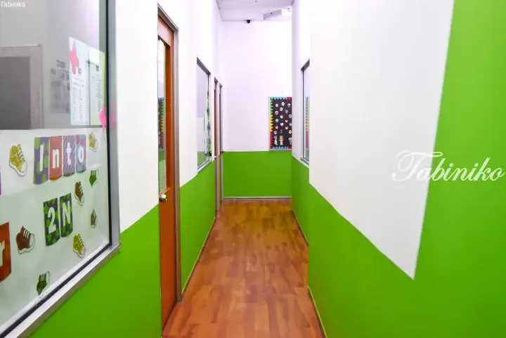 Bright hallway with green and white walls, wooden flooring, and classroom windows in a Malaysian school.