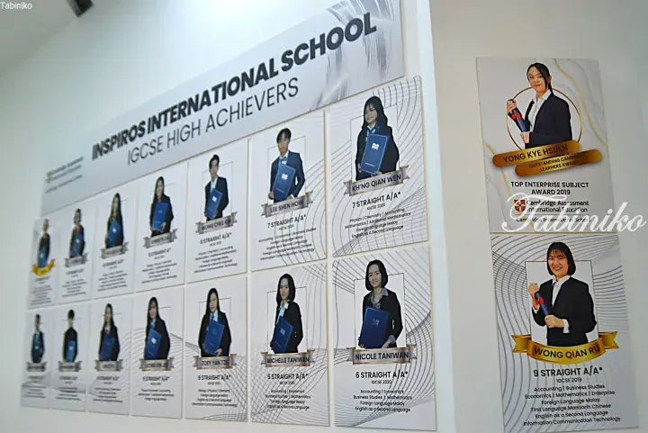 Wall display at Inspiros International School showcasing IGCSE high achievers with student photos and academic awards.