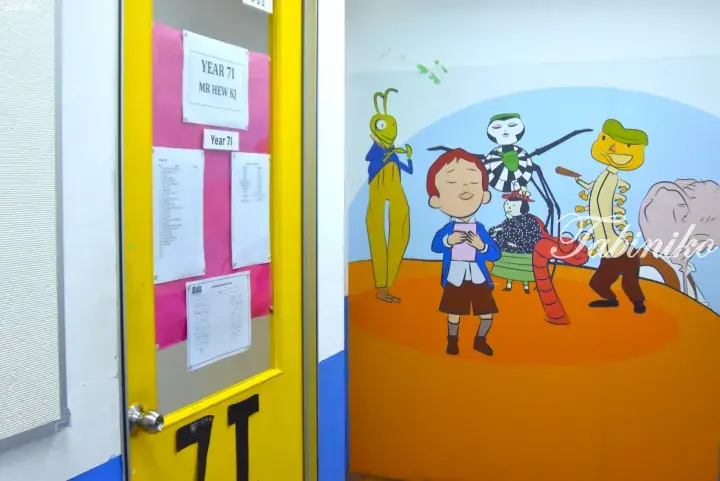 Yellow classroom door for Year 7I with teacher Mr Hew KJ&rsquo;s name, next to a colorful wall mural of animated characters.