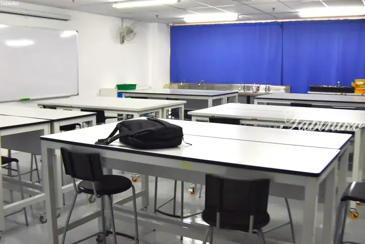 Modern science laboratory with white tables, black chairs, and a blue curtain backdrop.