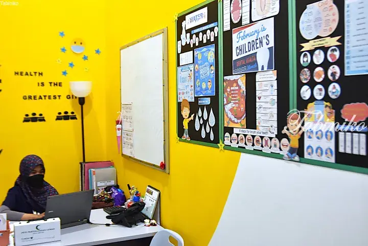 Reception desk with staff in a bright yellow school health clinic featuring dental health posters.