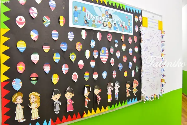 School bulletin board decorated with colorful paper balloons showing international flags and &lsquo;Welcome&rsquo; in various languages for International Day.