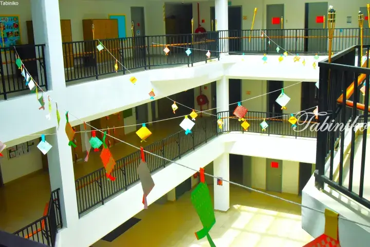 Colorful handmade decorations hanging across a bright multi-level atrium walkway in a modern building.