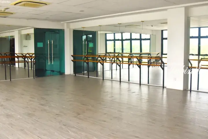 Spacious dance studio with wooden floors, mirrored walls, and ballet barres in a modern facility.