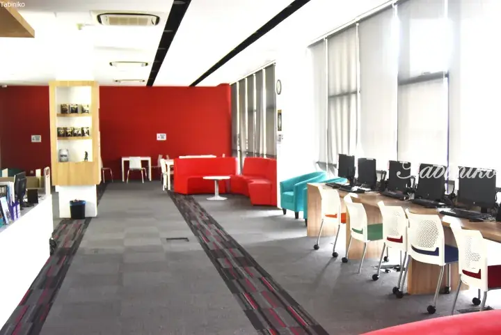 Modern library interior with red seating, computer workstations, and bright windows.