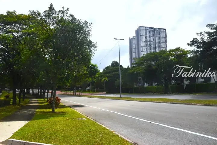 Tree-lined road with a tall residential apartment building in the background, showcasing a modern Malaysian property setting.