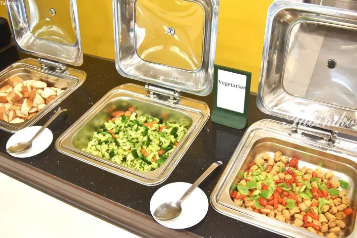 Buffet serving trays with vegetarian options including steamed broccoli, tofu stir-fry, and bread cubes.