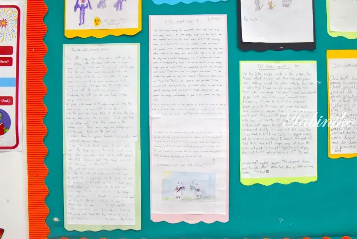Classroom bulletin board displaying children&rsquo;s handwritten stories and drawings on colorful paper.