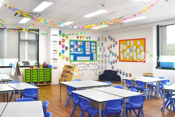 Bright classroom with blue chairs, educational posters, and colorful paper chains hanging from the ceiling.
