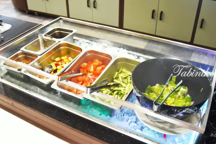 Fresh salad bar with tomatoes, cucumbers, lettuce, and fruit on ice at a buffet.