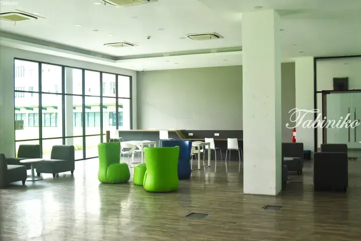 Bright modern lounge area with green and blue chairs, white tables, and large windows in a Malaysia property.