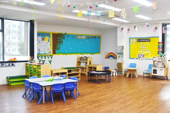 Bright preschool classroom with wooden floors, colorful learning stations, and Malaysian flags hanging from the ceiling.