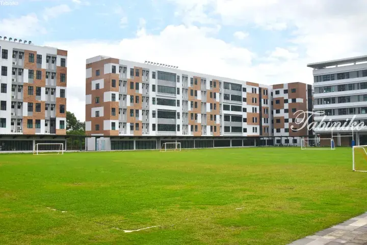 Modern brick and white campus buildings surrounding a green soccer field with goalposts.
