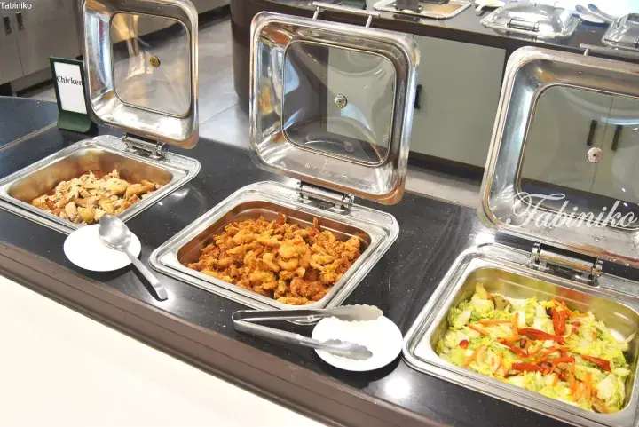 Buffet trays with chicken, fried shrimp, and vegetables at a hotel dining area.