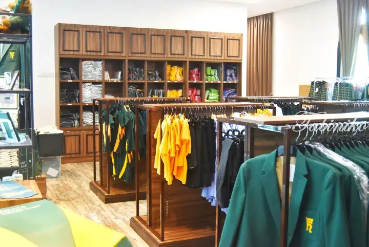 Interior of a school uniform shop displaying green blazers and yellow shirts on wooden racks.