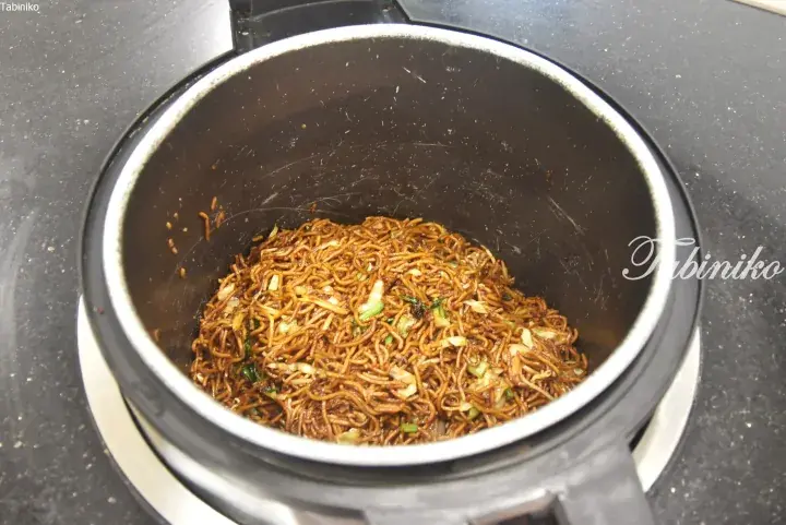 Cooked noodles with vegetables inside a black cooking pot.