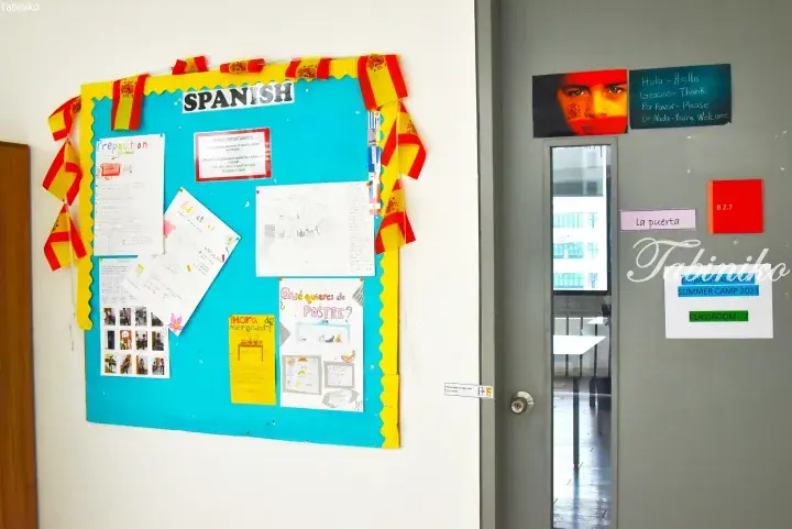 Spanish language bulletin board with student work and classroom door labeled &lsquo;Embassy Alliance Summer Camp 2023&rsquo;.