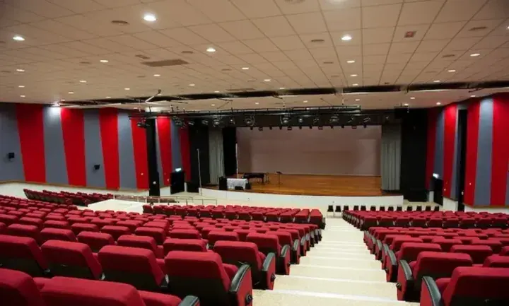 Empty auditorium with red seats and a wooden stage for events.